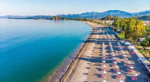 Dalaman Havalimanı'ndan Fethiye Çalış Plajı bölgesine VIP ulaşım sağlayan lüks Mercedes Vito araç, arkaplanda Jiva Beach Resort'un lagün manzarası ve meşhur Çalış gün batımı.