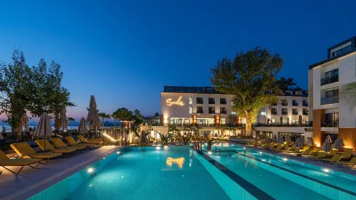 Dalaman Havalimanı'ndan Sundia Exclusive by Liberty oteline VIP transfer hizmeti veren siyah lüks Mercedes Vito araç, arkaplanda Çalış sahil kordonu ve modern otel cephesi.